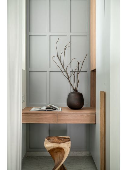 Even a small nook can become a beautiful and functional space. This compact study area features a floating oak desk set against a grey paneled wall, with a sculptural wooden stool adding an artistic touch.