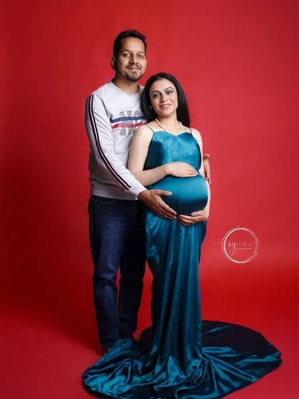 A classic standing pose for a maternity couple's portrait. This shot beautifully showcases the baby bump and the supportive embrace of the partner against a simple, bold background.