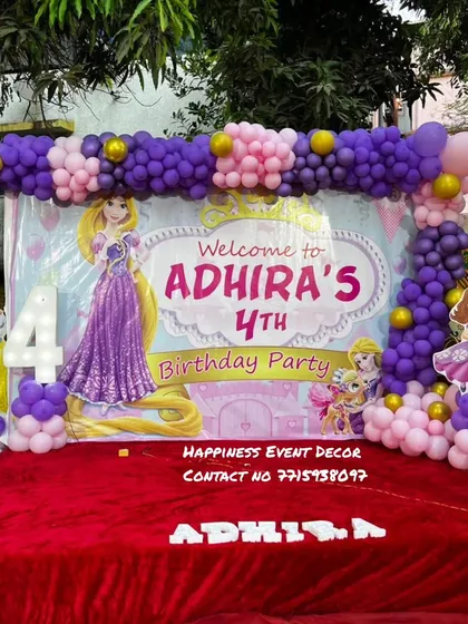 A Rapunzel-themed 4th birthday party stage. The decor uses a custom banner and a purple and pink balloon arch to match the princess's colors.