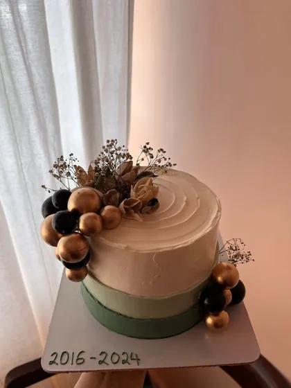 A modern and sophisticated farewell cake. This design features an olive green and white ombre effect, decorated with a cascade of black and gold spheres and dried florals.