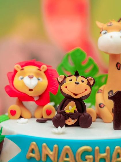 A delightful jungle-themed cake for a first birthday. This cake is topped with adorable, handcrafted fondant animals including a lion, monkey, and giraffe, perfect for a wild adventure party.