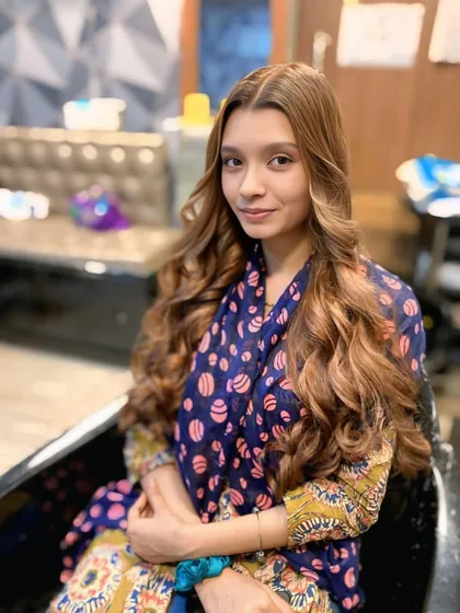 A stunning hair transformation featuring a warm, caramel balayage on long hair, styled with soft, flowing curls.