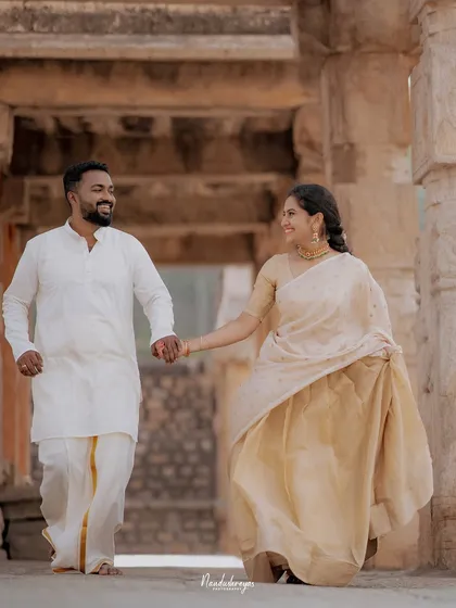 Hand in hand, a couple walks through a stone corridor at Melukote, sharing a look of love and laughter. I focus on these natural interactions that tell your true story.