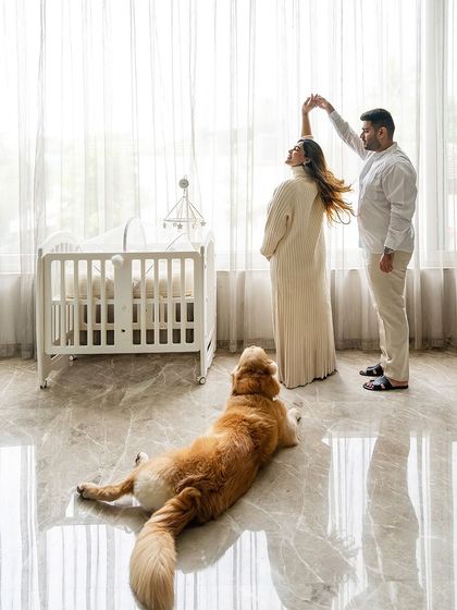 A beautiful, wide shot of a couple dancing by the window near a crib, while their Golden Retriever, Hugo, lies peacefully on the floor, watching over them.