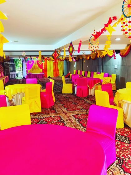 This photo shows the seating arrangement with bright pink and yellow chair covers and round tables, ready for guests at a Janmashtami event.