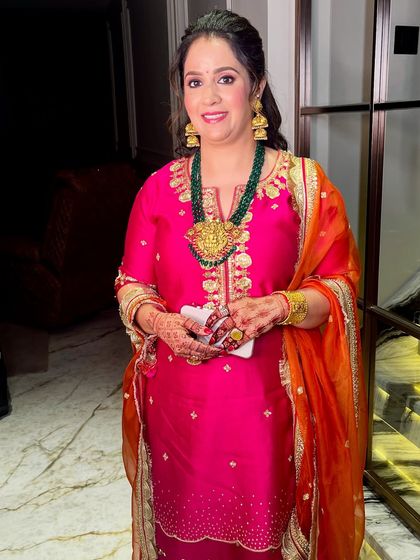 The full look, a vibrant pink and orange suit paired with traditional gold jewelry.