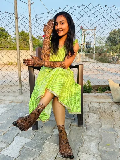 A happy bride enjoying the sun with her full bridal mehendi. The dark, rich stain of the natural henna is clearly visible on both her hands and feet.