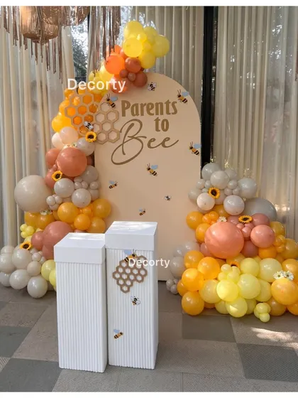 A sweet 'Parents to Bee' themed baby shower backdrop. The decor uses a warm yellow and orange color palette with honeycomb patterns and cute bee accents.