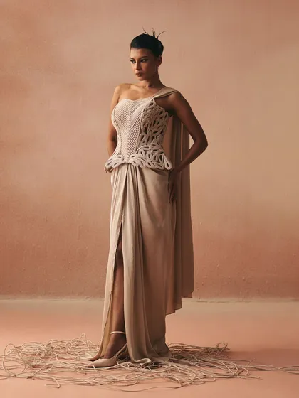 This draped gown features a one-shoulder silhouette and a thigh-high slit, with a structured, cord-embroidered corset that adds a sculptural element to the fluid design.