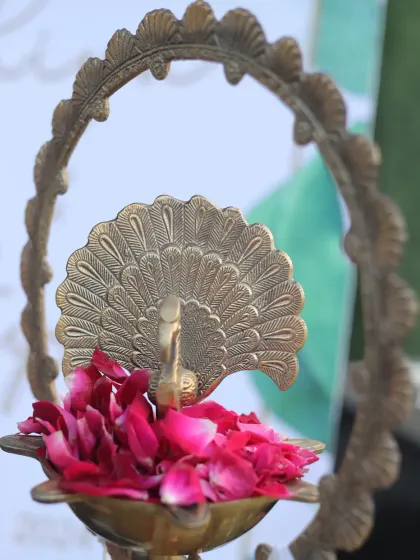 A traditional brass peacock diya filled with fresh rose petals serves as a beautiful and symbolic welcome element. This small detail adds a touch of grace and auspiciousness to the entrance of any spiritual gathering or wedding.