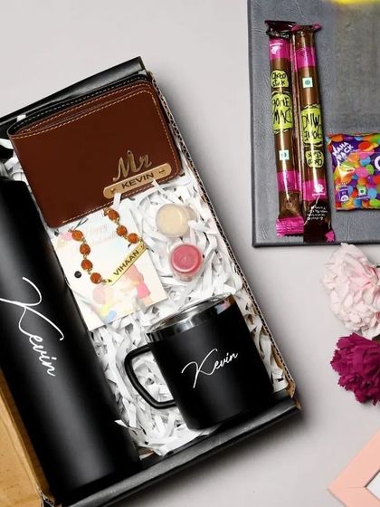 This premium Rakhi combo includes a personalized bottle, a black metal mug, a Rudraksha name rakhi, a custom wallet, and chocolates, all packed in a gift box.