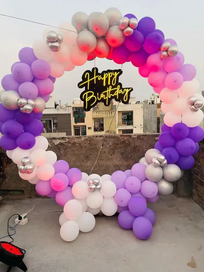 We can transform any space, including a terrace with a city view. This outdoor birthday setup features a full balloon ring in shades of purple, lavender, and white, with a central neon sign, proving that a great party can happen anywhere.