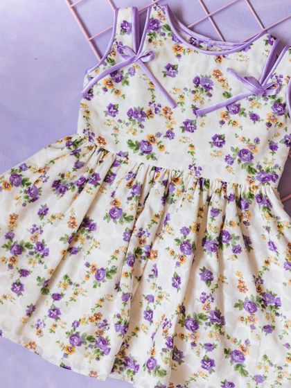 A lovely white dress with a purple floral print and shoulder-tie details, perfect for a warm summer day.