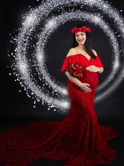 A stunning portrait in a red lace mermaid gown. The sparkling light effect adds a touch of magic, perfectly framing the mom-to-be and her floral accessories.