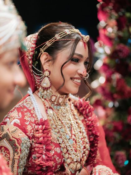 A radiant smile from a beautiful bride. Her makeup is a blend of tradition and timeless elegance, with softly defined eyes and glowing skin that looks perfect with her red lehenga.