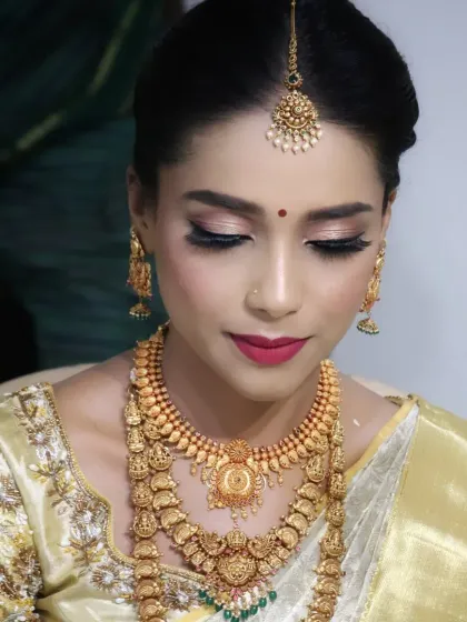 A beautiful close-up showcasing the intricate details of a South Indian bridal look. The eye makeup is soft yet defined, and the traditional gold jewellery, including the maang tikka and necklaces, completes the look.