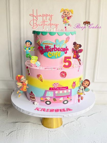 A sweet and colorful two-tier cake based on Butterbean's Café. This whimsical design is filled with fairies, ice cream, and macarons, perfect for a magical 5th birthday.