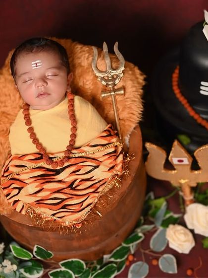 A newborn Bala Shiva setup, with the baby sleeping in a basket next to a Shivling prop.