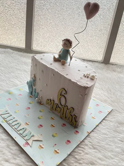 A simple and sweet half-cake for a 6-month-old, featuring a little baby topper holding a heart balloon.