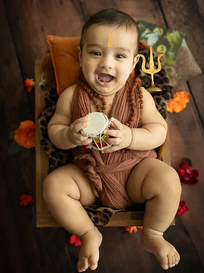 The baby joyfully holds a small damaru, adding an authentic touch to his divine costume.