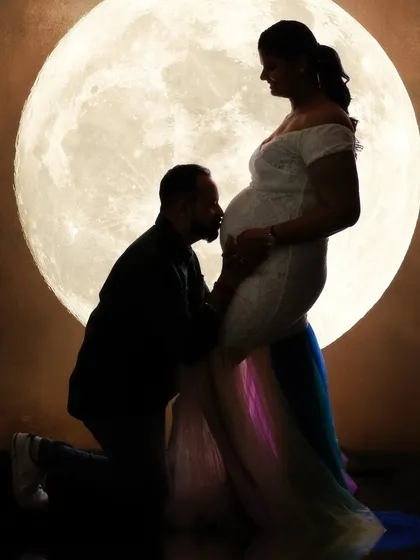 Bathed in moonlight. This dramatic silhouette captures a father's loving kiss against a glowing full moon. It's a powerful, artistic image that symbolizes the cosmic scale of their love and new life.