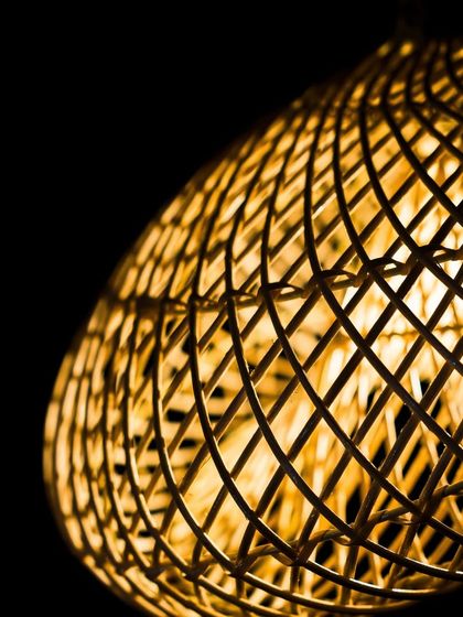 A close-up of the sculptural lamp's intricate weave. The complex, crisscrossing lines of rattan demonstrate a mastery of the craft and create a visually stunning texture.