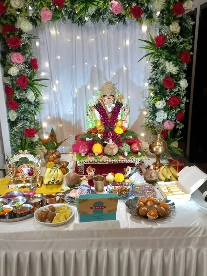 This is a complete view of our popular rose arch decoration in a client's home. The frame of red, pink, and white roses with green leaves, paired with a simple curtain and fairy lights, creates a full and festive space for Bappa and all the puja offerings.