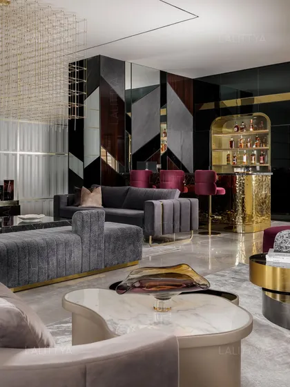 This perspective highlights the custom bar unit, featuring an arched, illuminated display for spirits and a hammered brass front. The design seamlessly connects the bar with the main lounge, which includes plush grey sofas and a unique marble-topped coffee table.
