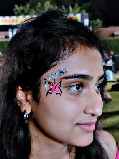 A small pink butterfly on the forehead, highlighted with a sweep of silver glitter.