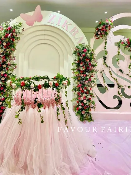 A magical butterfly-themed Aqeeqah for baby Zikra. The centerpiece is a cradle decorated with a pink tulle skirt and fresh flowers, set against elegant white arched backdrops.