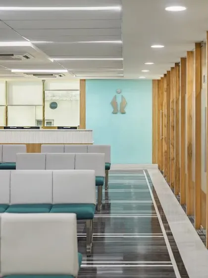 This waiting area uses biophilic design principles, with wooden partitions and planters creating a connection to nature. The soft green seating and natural light from the corridor enhance the calming, restorative quality of the space.
