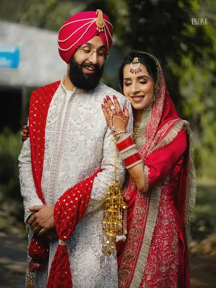A classic portrait of a Sikh couple. The bride's hand on her groom's shoulder and their happy expressions showcase their connection and the beauty of their traditional attire.