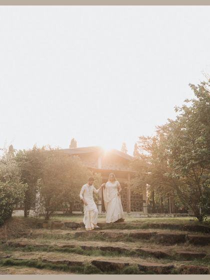 A wide shot of the couple walking hand-in-hand in a rustic, natural setting, with the sun setting behind them.