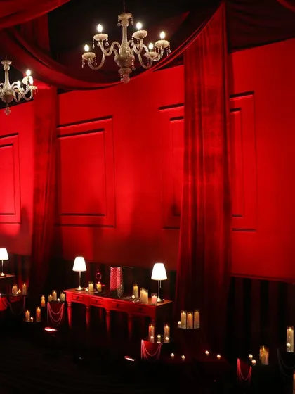 Ambiance is in the details. For our 'Scarlet Splendor' theme, we transformed a large space into an intimate, luxurious lounge with rich red draping, classic chandeliers, and hundreds of candles to create a warm, opulent glow.
