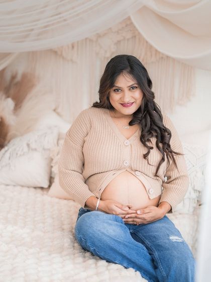 A warm and cozy portrait on our studio bed. The mom-to-be, in a comfortable knit cardigan and jeans, smiles warmly, creating a relaxed and inviting image.
