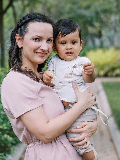 A mother and son portrait in a lush green setting. The soft light and her gentle hold create a peaceful, loving image.