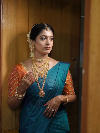A pensive moment for the bride before her ceremony. The lighting here showcases the smooth finish of the HD makeup and the richness of her teal and orange silk saree.