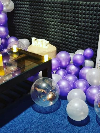 A cozy corner of an anniversary setup, with purple and white balloons, a 'LOVE' sign, and LED candles creating an intimate atmosphere.