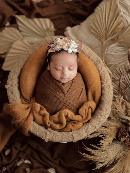A beautiful newborn portrait with a bohemian touch. The earthy tones, dried leaves, and floral headband create a natural and warm feel.