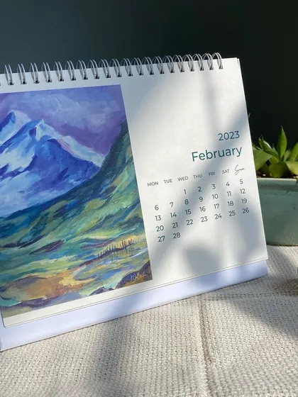 The February page of my art calendar, showcasing a dramatic acrylic painting of blue and purple mountains. Each month offers a new piece of art to brighten your desk.