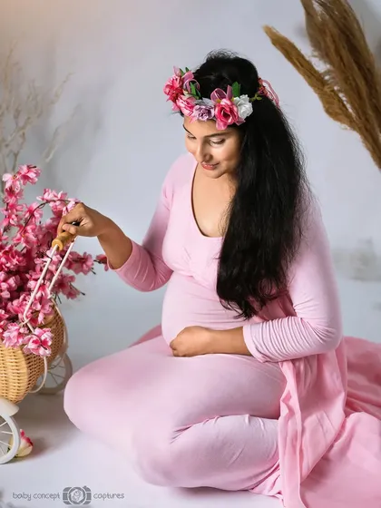 A beautiful seated portrait of a woman in a flowing pink gown, wearing a floral crown. She is interacting with a basket of pink blossoms, creating a soft, feminine, and spring-like atmosphere.