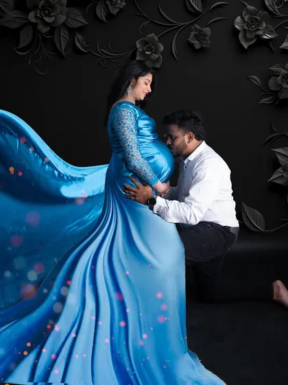 A powerful and romantic portrait of expectant parents. The deep blue flowing gown creates a stunning visual against the dark, moody backdrop, highlighting the connection between the couple as they await their baby.