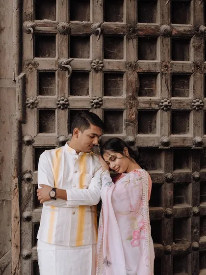 A quiet, romantic moment against an intricately carved wooden door, a classic backdrop in Udaipur. The couple's gentle pose and traditional wear evoke a sense of timeless elegance.