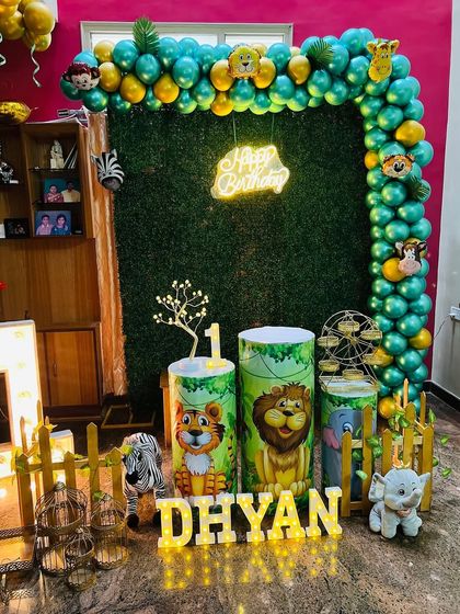 The complete jungle safari first birthday setup, featuring a grass wall, balloon arch, themed pedestals, props, and light-up name and number.