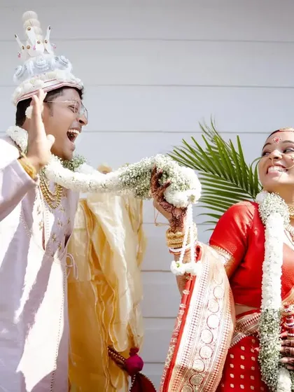 A playful moment during a Bengali wedding's Varmala ceremony. The genuine laughter and joy are perfectly captured.