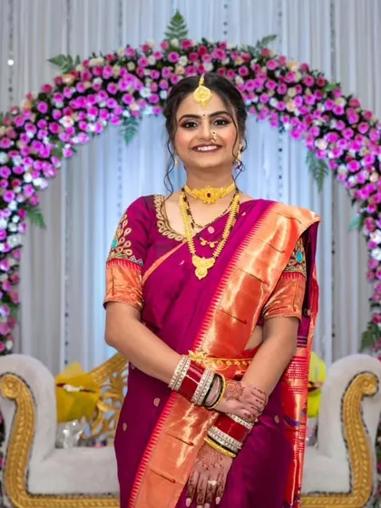 A traditional Maharashtrian reception look. The bride's rich purple Paithani saree is paired with gold jewelry and classic makeup, including a crescent bindi.
