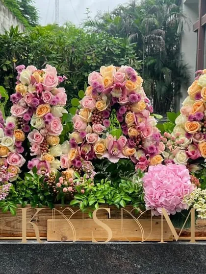 For a milestone birthday, I created this 'MAA' arrangement with big love. Using a palette of pinks and peaches, this floral sculpture combines roses, hydrangeas, and lilies in a custom wooden box for an immense display of joy.