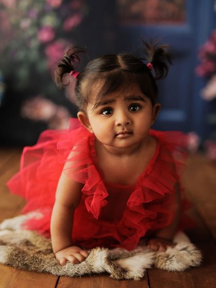Two little pigtails add to the cuteness. This is a beautiful, painterly portrait of a toddler against a floral backdrop.