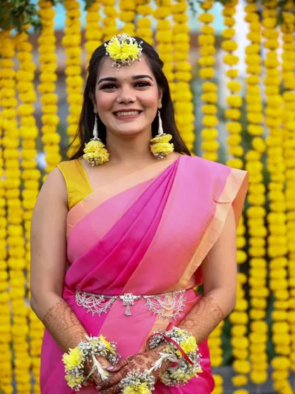 A simple and sweet Haldi look. The bride wears a pink and yellow saree with fresh floral jewelry, and her makeup is kept minimal and glowing.