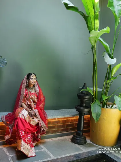 A serene solo portrait of the bride seated, her red wedding outfit vibrant against the cool green background.